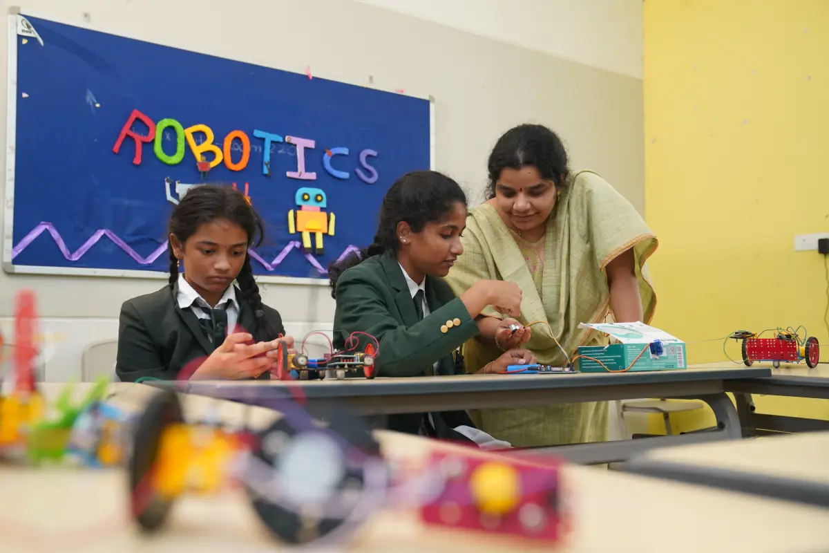 Teacher in a light green suit teaching students robotics in the robotic lab.