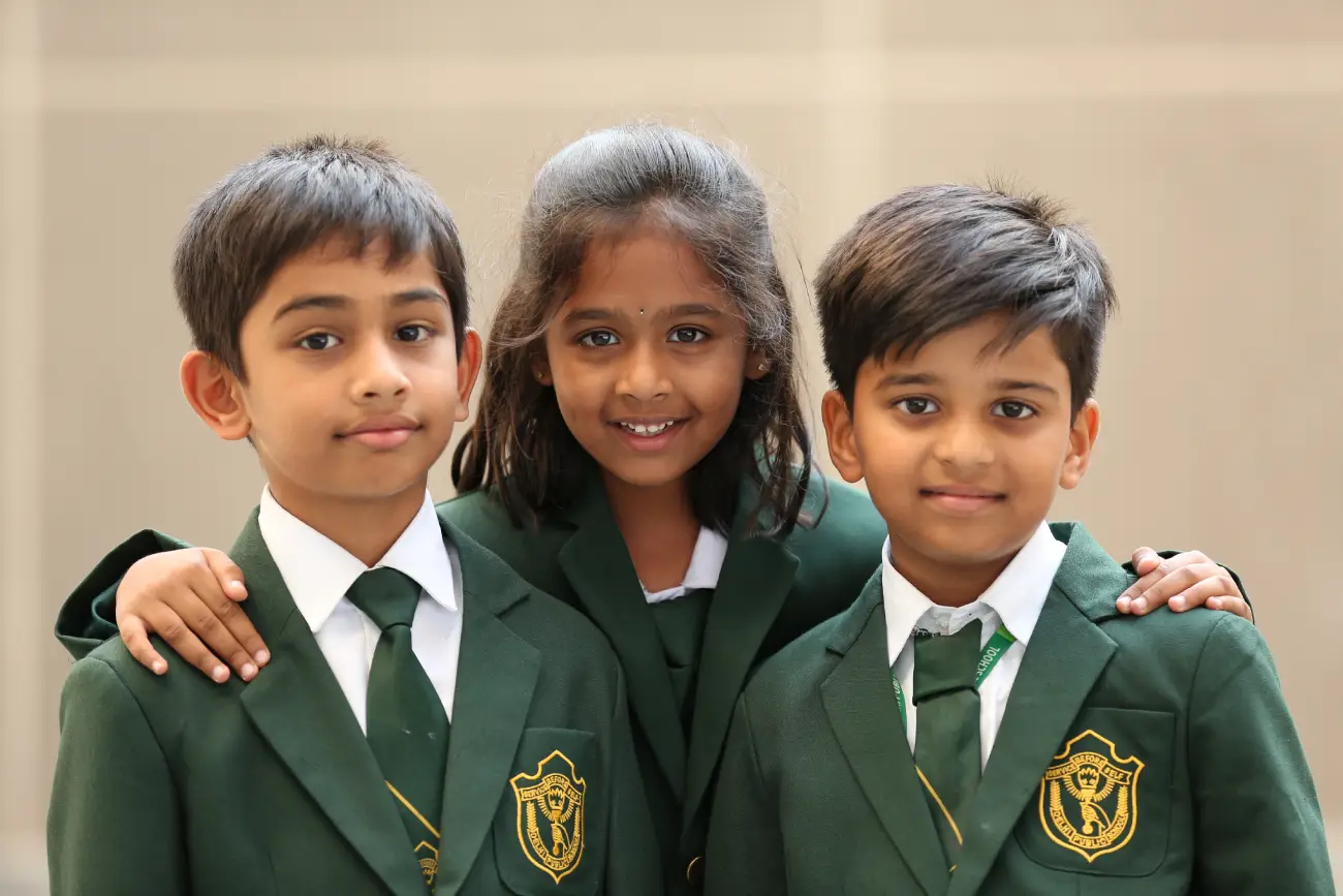 Two boys in the corner and one girl in the middle smiling in a white-green school uniform.