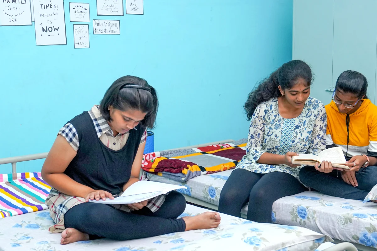 Three girls studying in the hostel room, helping each other in their studies.