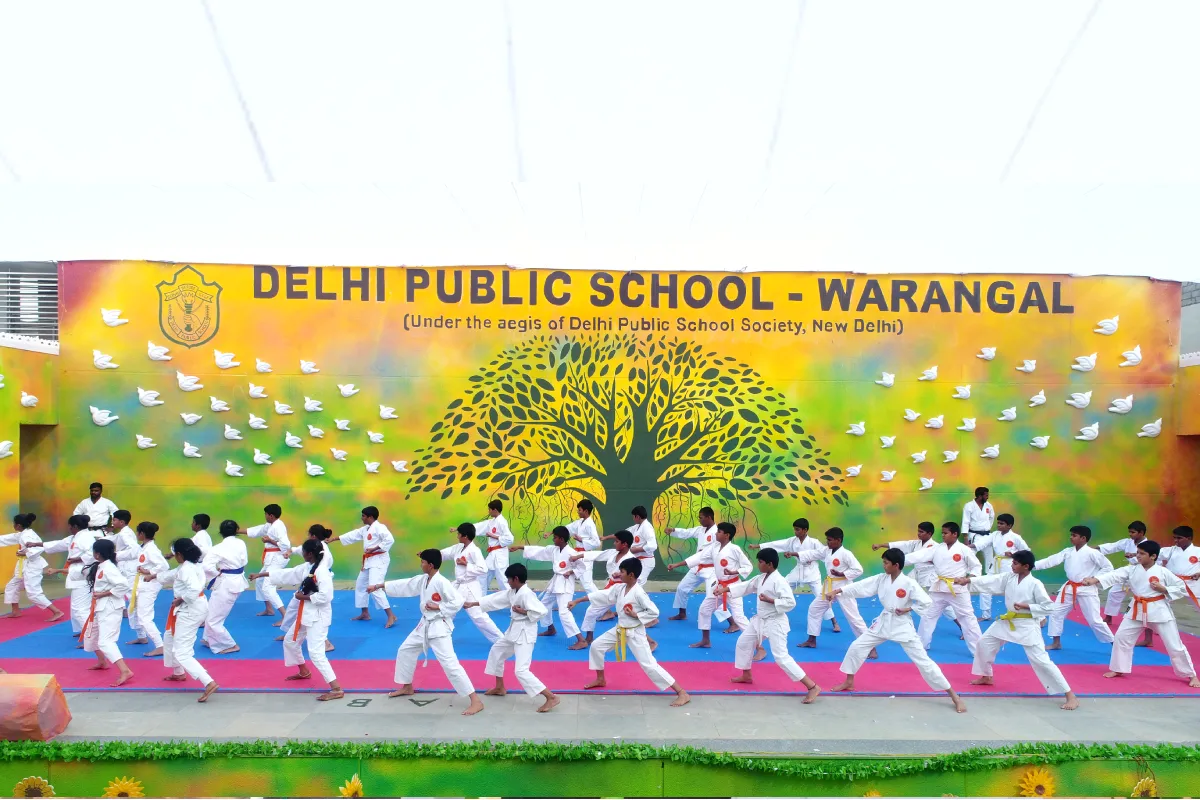 Students of DPS Hanamkonda Warangal displaying karate moves on stage in white karate uniform.