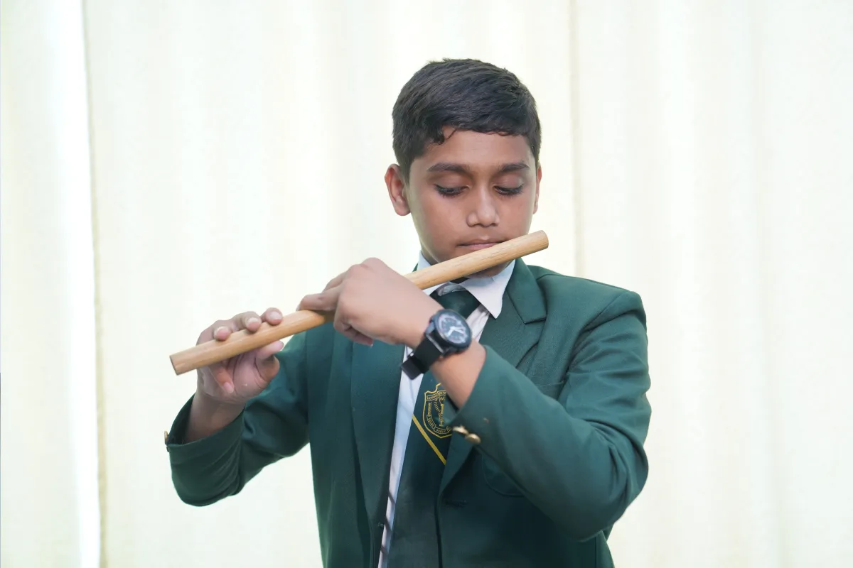 A student in a school uniform at Delhi Public School, Warangal is playing the flute.