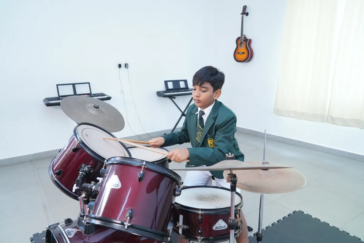 A child in a school uniform at DPS, Warangal is playing the drum in the music hall.