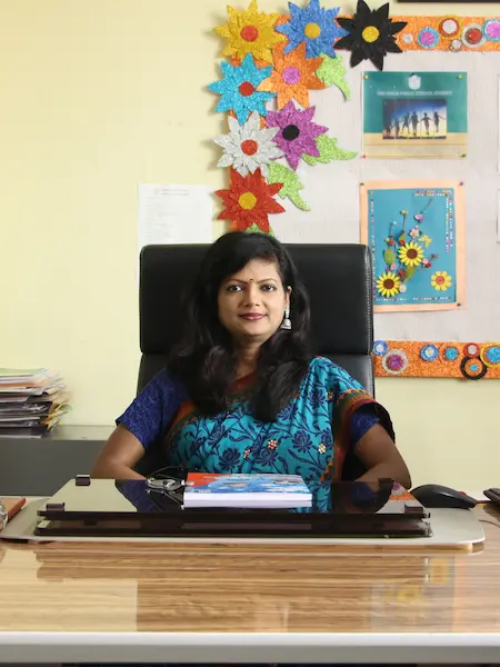 Principal Pillai Manjumol Shivashankar of DPS Warangal School, sitting behind her desk, at school, wearing a blue saree.