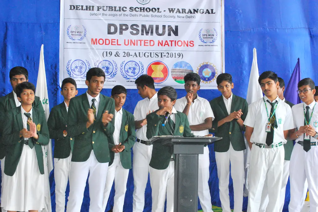Student delivering speech at DPS Warangal Model United Nations conference and other students in school uniform appreciating him.