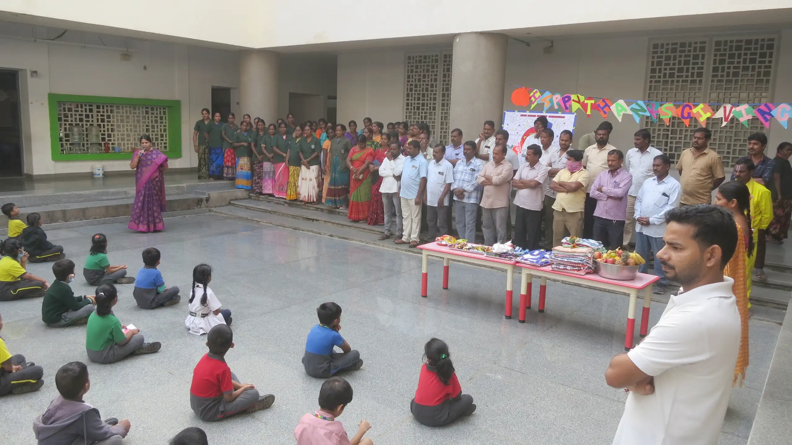 Students sitting in the floor and listening to teacher during thanks giving celebration at DPS Warangal.
