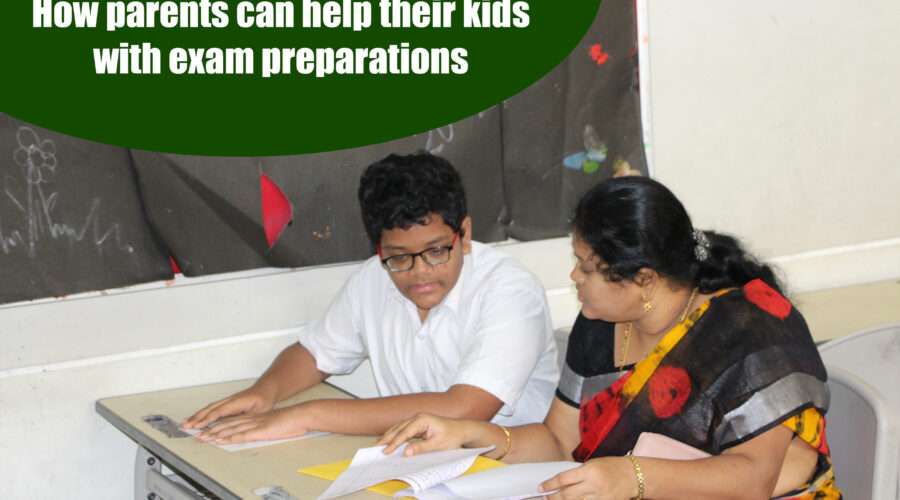 A young boy wearing glasses and a white shirt sits at a desk, preparing for his exam with his mother wearing a sari