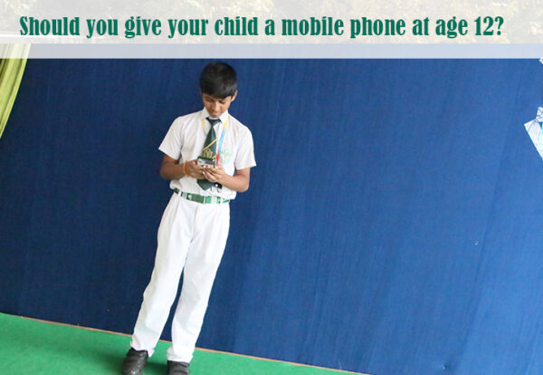 A child standing against a blue background, holding a mobile phone.