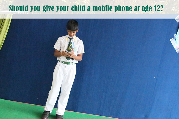 A child standing against a blue background, holding a mobile phone.