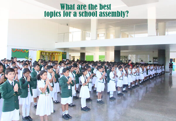 Students standing in rows with hands clasped, participating in a school assembly.